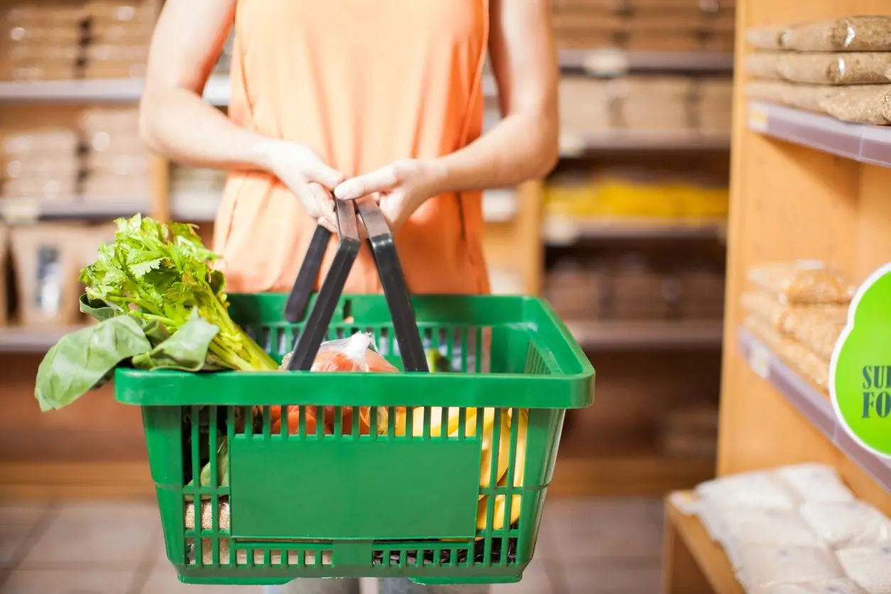 Closeup of a young woman holding a basket full of groceries and organic healthy food in a supermarket